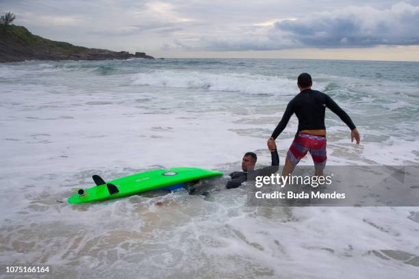 Andre Melo de Souza or Andrezinho Carioca receives the help of a friend surfer Felipe "Badezir" at Prainha beach on December 26, 2018 in Rio de...