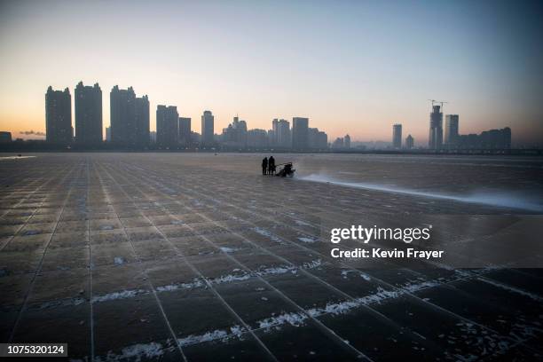 Chinese workers use use a machine to cut into large blocks of ice that will be used in the making of ice sculptures from the frozen Songhua River in...