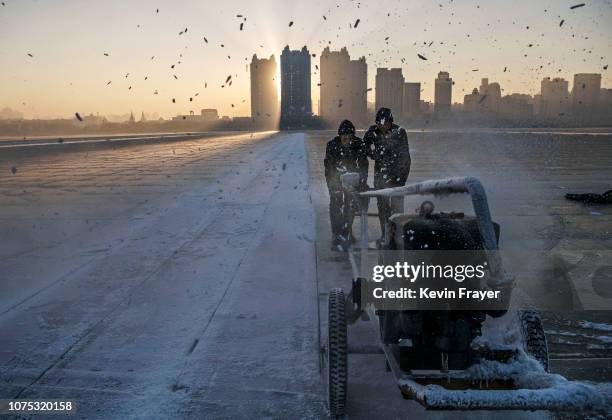 Chinese workers use use a machine to cut into large blocks of ice that will be used in the making of ice sculptures from the frozen Songhua River in...