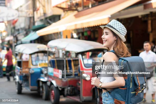 young woman traveling with hat, asian hipster traveler walking at famous backpacker street in bangkok (khao san road), landmark and popular for tourist attractions in thailand. travel concept - rucksacktourist stock-fotos und bilder