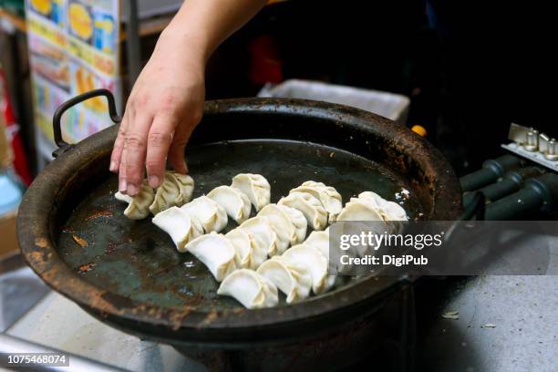 market vendor man putting dumplings into fry pan - chinese dumpling stock pictures, royalty-free photos & images