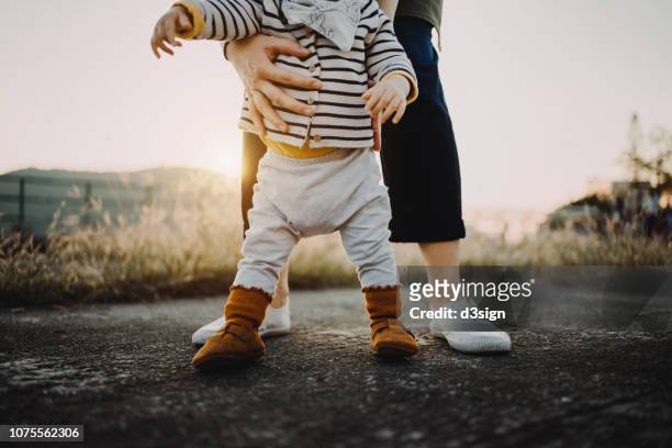 mother holding baby daughter's body helping her to take her first step in life - baby boy and girl stockfoto's en -beelden
