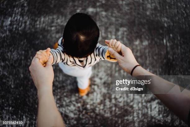 overhead view of mother holding baby daughter's hand helping her learn to walk - moments daily life from above stock-fotos und bilder