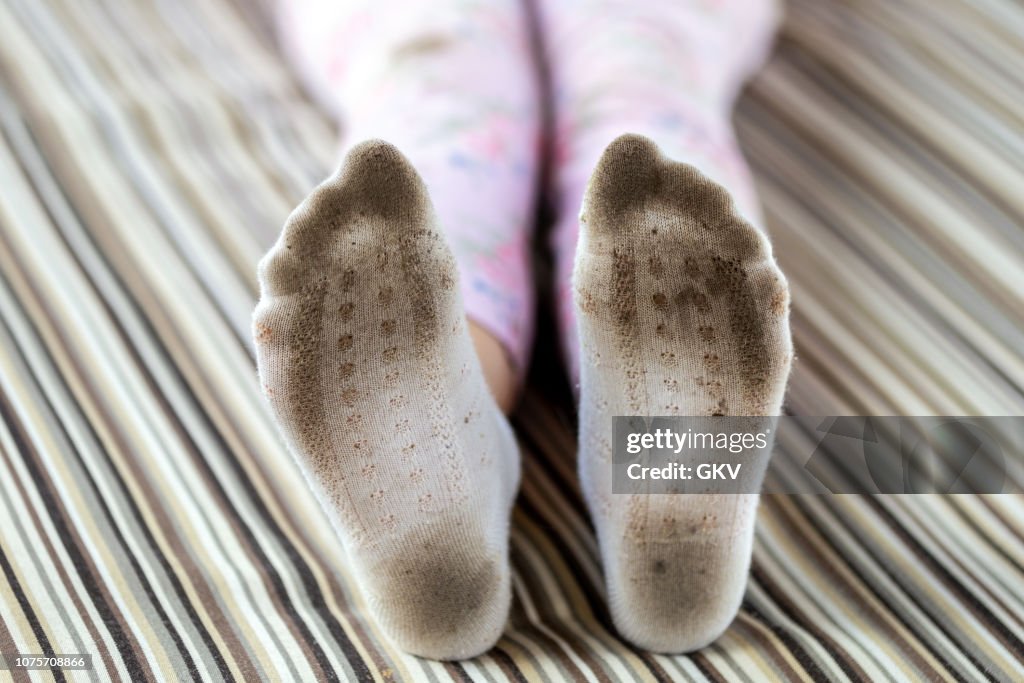 Pair of child feet in dirty stained white socks. Kid soiled socks while playing outdoors. Children clothes bleaching and washing troubles concept