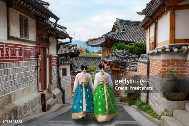 back of two woman wearing hanbok walking through the traditional style houses of bukchon hanok village in seoul, south korea. - corea del sur fotografías e imágenes de stock
