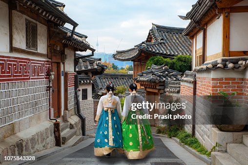 Back of two woman wearing hanbok walking through the traditional style houses of Bukchon Hanok Village in Seoul, South Korea. Back of two woman wearing hanbok walking through the traditional style houses of Bukchon Hanok Village in Seoul, South Korea.