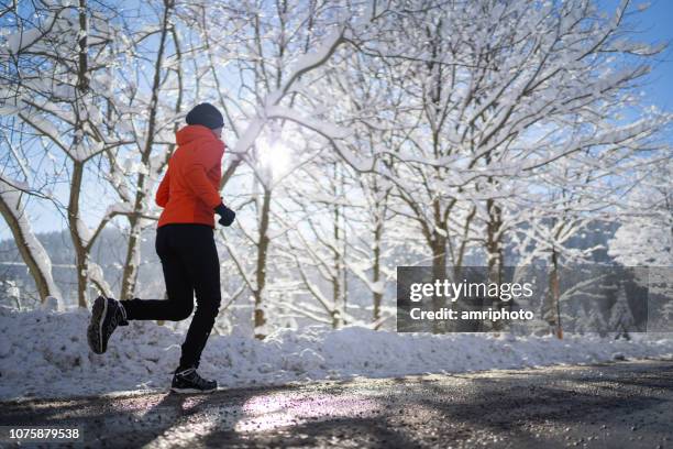 side view woman jogging running on road cold sunny winter day - winter running stock pictures, royalty-free photos & images