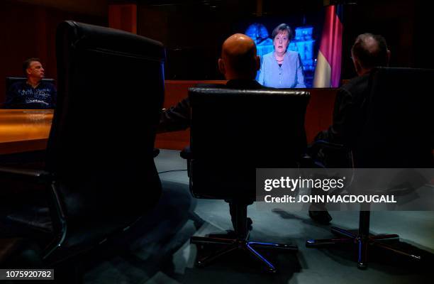 Chancellery officials and media technicians watch a monitor showing German Chancellor Angela Merkel as she delivers her annual New Year's speech in...