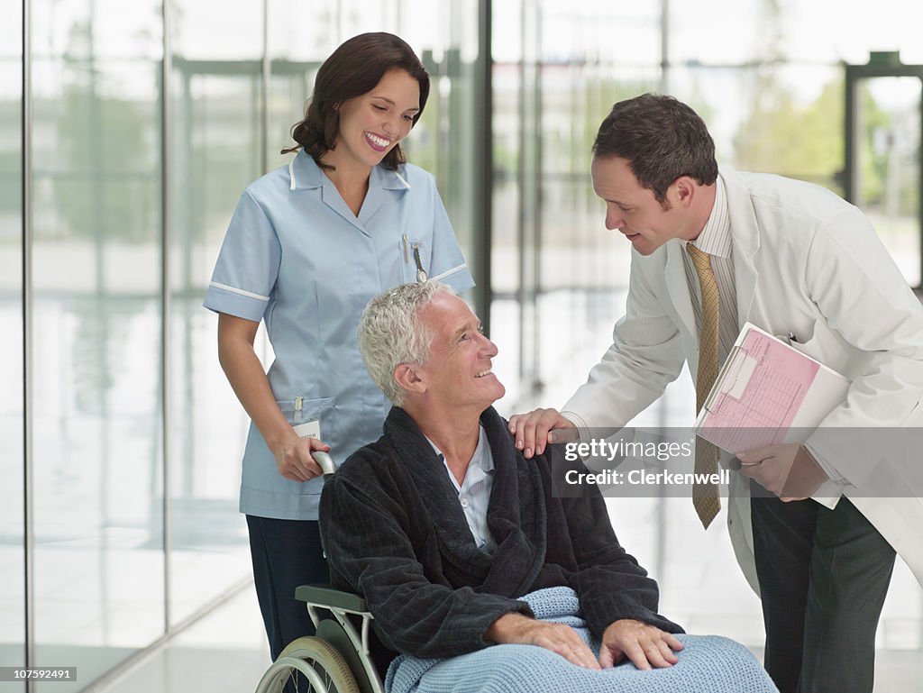 Senior patient on wheelchair with male doctor and female nurse in hospital