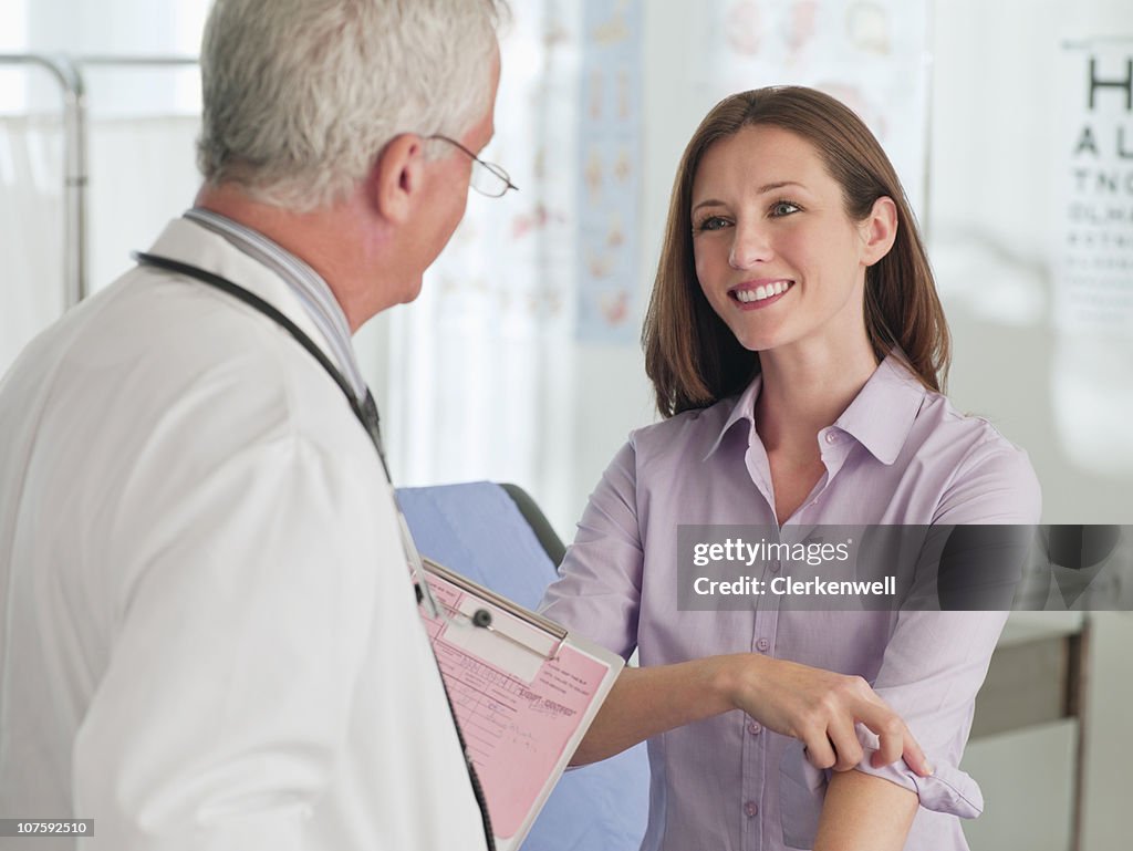 Smiling woman folding her sleeves while talking to a doctor