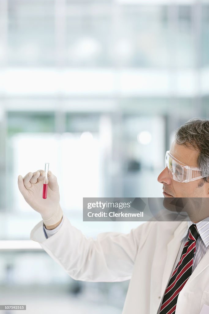 Male doctor wearing protective eyewear while and holding test tube
