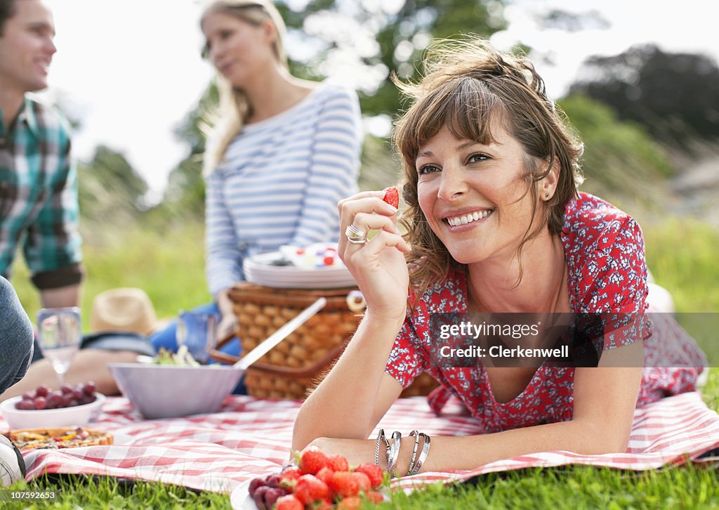 Happy woman holding strawberry with friends sitting together during picnic