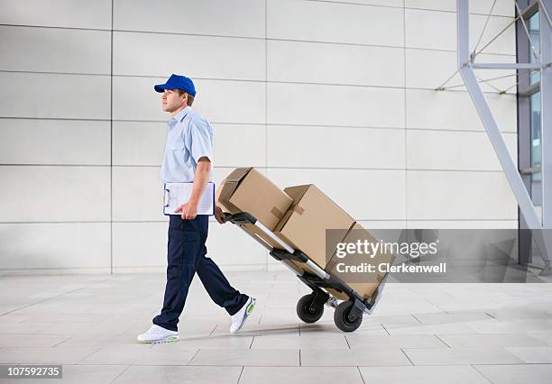 livraison homme évacue panier de colis à travers le bureau du hall - diable-chariots-et-charrettes photos et images de collection