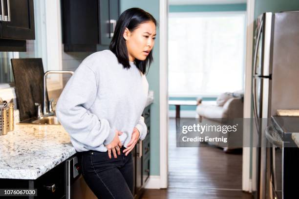 a young woman experiencing pelvic discomfort, she is grimacing in pain. - groyne stock pictures, royalty-free photos & images