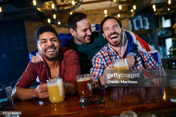 group of young joyful friends having fun while toasting with beer in a pub - lager stock pictures, royalty-free photos & images