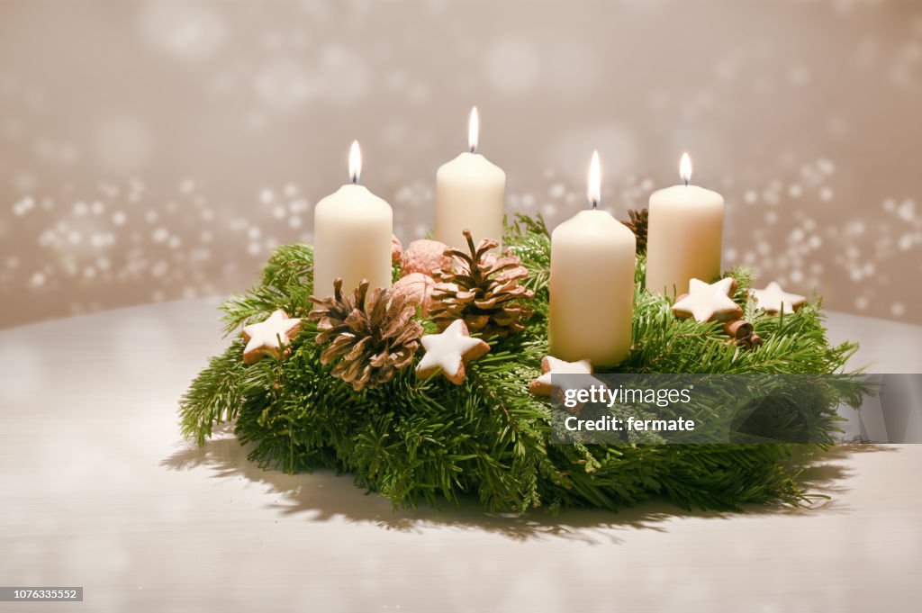 Fourth  Advent - decorated Advent wreath from fir and evergreen branches with white burning candles, tradition in the time before Christmas, warm background with festive bokeh and copy space