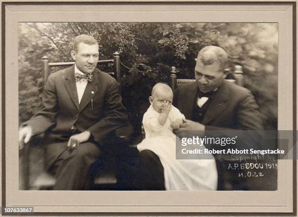 American educator, economist, and industrialist Booker T Washington holds his grandson on his lap, while sitting next to his son, circa 1915.