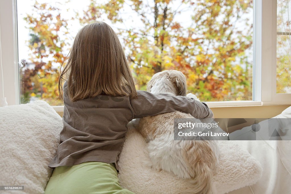 Young girl and her dog looking out the window