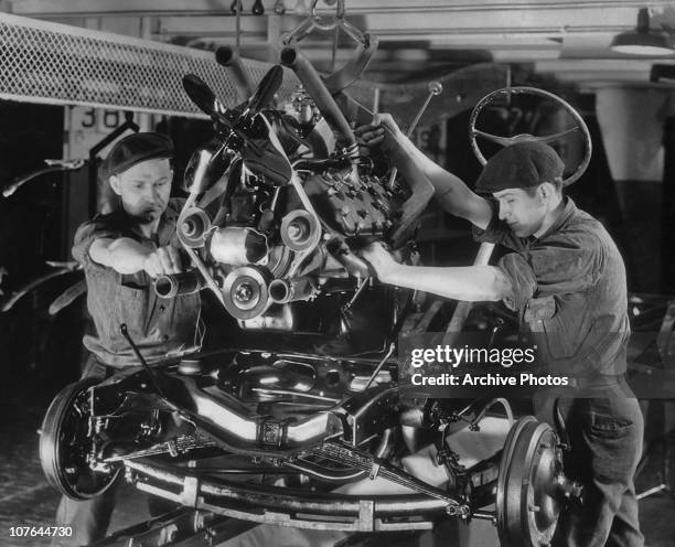 Workers lowering a V8 engine onto its chassis at a Ford car plant in the USA, circa 1935.