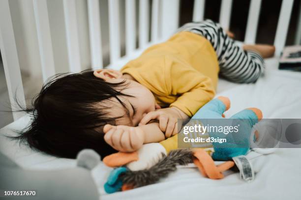 thumb sucking baby girl sleeping peacefully in crib with a plush toy - stuffed toy stock pictures, royalty-free photos & images