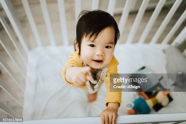 adorable asian baby girl standing in her crib and pointing away with fingers - baby pointing stock pictures, royalty-free photos & images