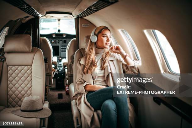 young fashionable woman sitting on a private airplane and listening to music through headphones - rich celebrities stock pictures, royalty-free photos & images