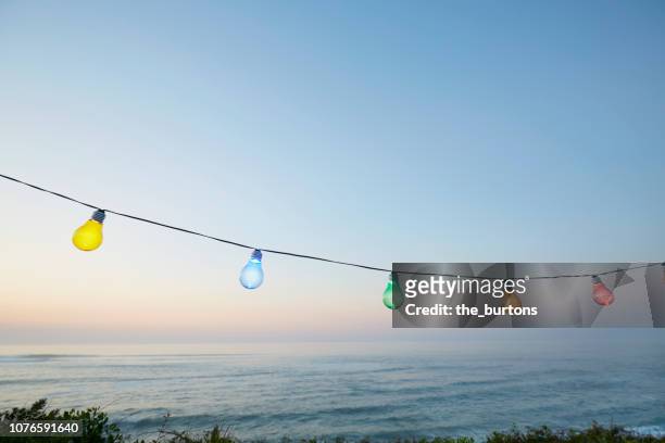 colorful string lights for party decoration against sea and sky during sunset - summer party photos et images de collection