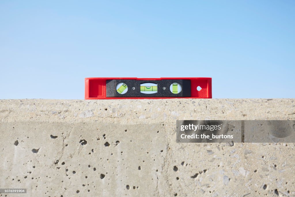 Still life of red spirit level on concrete wall against blue sky