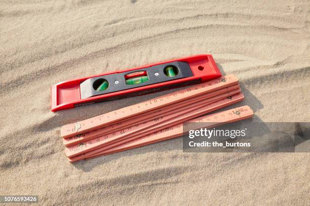 high angle view of a red folding ruler and spirit level on sand/ construction site - duimstok stockfoto's en -beelden