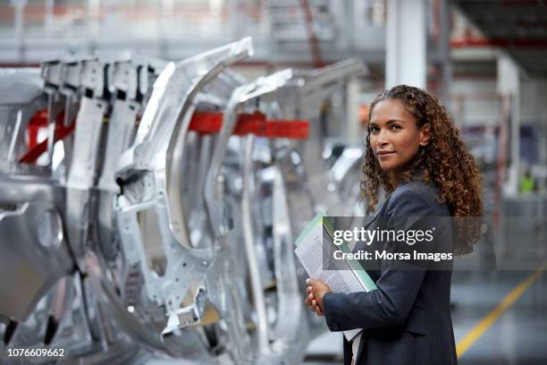 confident manager standing by chassis in car plant - robotic car stock pictures, royalty-free photos & images