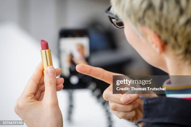 Posed scene on the topic of influencers. A woman holds a lipstick in her hand and films herself with her smartphone on January 03, 2019 in Berlin,...