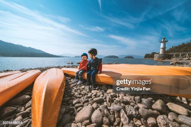 portrait of the brothers wearing sport helmet and sitting on a boat by the river - kids at river photos et images de collection