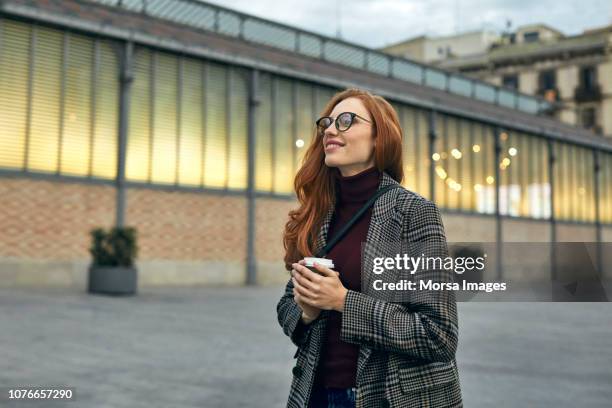 nachdenklich lächelnde frau mit einweg-becher - stylish man looking away stock-fotos und bilder