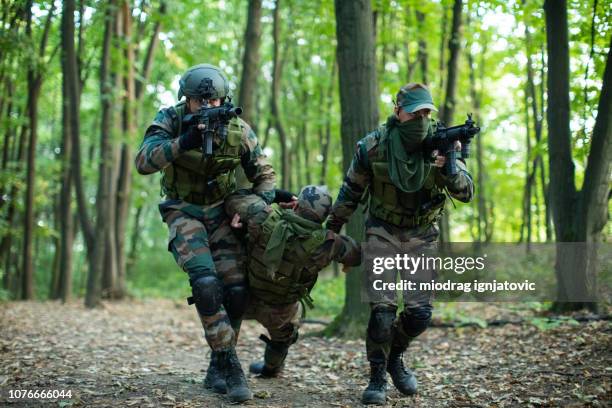 two soldiers helping their injured friend - injured soldier stock pictures, royalty-free photos & images