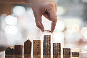 Hand choosing row of coin money on wood table and mini wood house, selective focus, Planning to buy property. Choose what's the best. A symbol for construction ,ecology, loan concepts