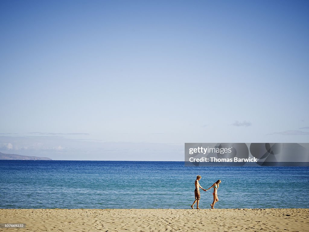 Couple holding hands walking on empty beach