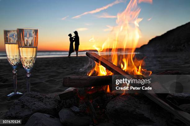 romantic couple, beach, fire and champagne - bonfire beach stock pictures, royalty-free photos & images