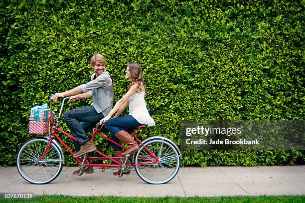 couple riding tandem bike in front of hedge - tandem bicycle stockfoto's en -beelden