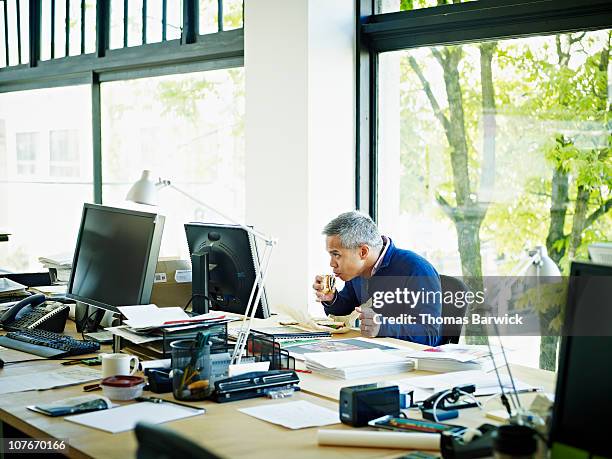 businessman taking bite of sandwich at desk - office lunch stock pictures, royalty-free photos & images