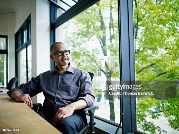 businessman sitting at desk looking out window - solo un uomo maturo foto e immagini stock
