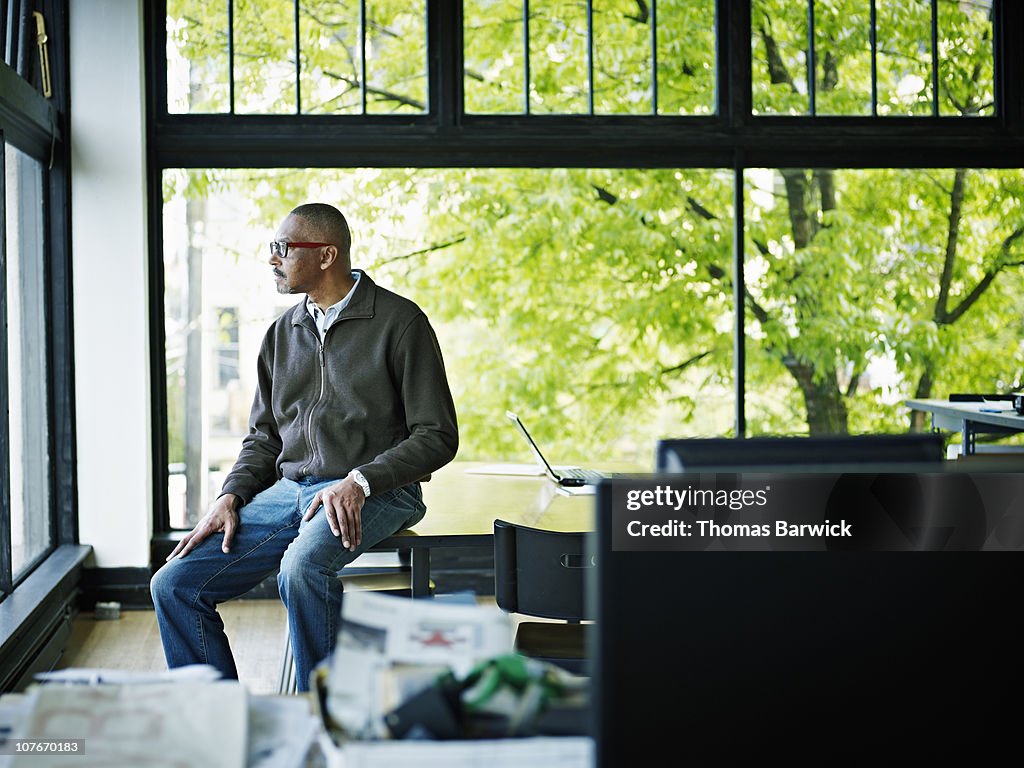 Businessman sitting on edge of table looking out