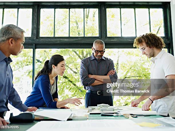 four architects examining plans at table in office - identity management stock pictures, royalty-free photos & images