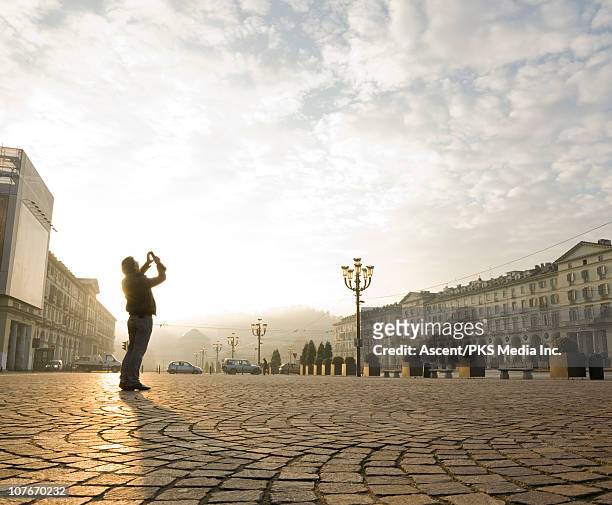 man stands in urban piazza, takes pic with cell - piazze italiane foto e immagini stock