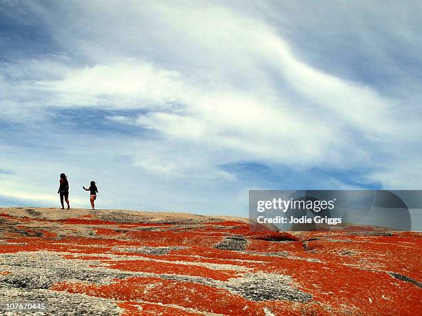 two people walking along red rocks - hiking tasmania stock-fotos und bilder