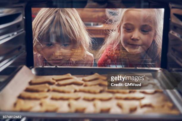 little girls waiting for christmas cookies to bake in the oven - baking stock pictures, royalty-free photos & images