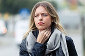Illness young woman with terrible throat pain walking to the street.