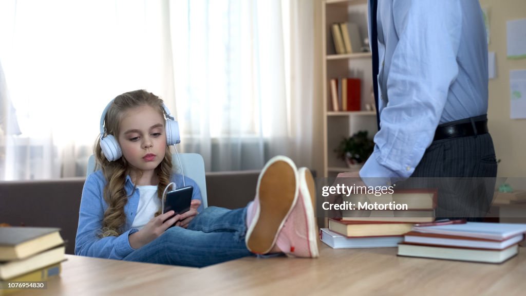 Menina desobediente em fones de ouvido, ouvindo música no smartphone, ignorando o pai