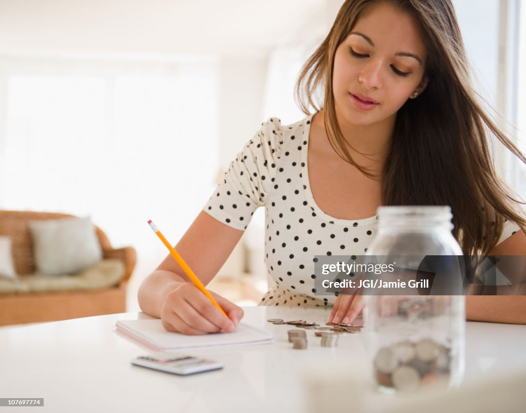 Indian woman counting coins and writing on notepad