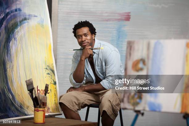 smiling black artist sitting in studio - male artist painting stock pictures, royalty-free photos & images