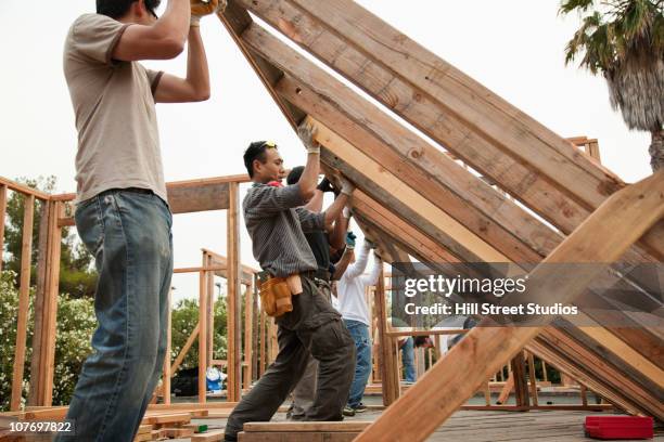 construction workers lifting house frame - madera material de construcción fotografías e imágenes de stock